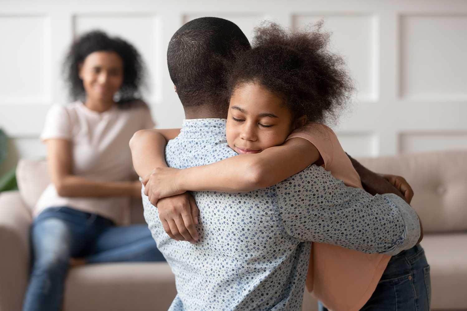 Black man embracing young Black girl with Black woman in the background smiling