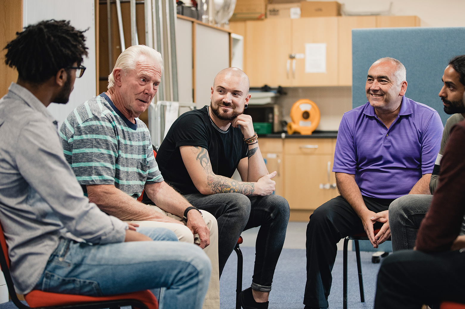 Senior white man sharing in a circle of other men who are listening to him and smiling in support